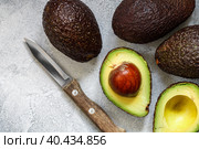 Whole and cut in half ripe organic avocados and a knife on a grey background. The Haas Avocado. Source of vitamins , trace elements , beta-carotene and omega-3 fatty acids . Healthy food, diet. Стоковое фото, фотограф Виктория Панченко / Фотобанк Лори