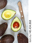 Whole and cut in half ripe organic avocados and a knife on a grey background. The Haas Avocado. Source of vitamins , trace elements , beta-carotene and omega-3 fatty acids . Healthy food, diet. Стоковое фото, фотограф Виктория Панченко / Фотобанк Лори