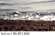 The edge of the coast is made of seashells and sand. Unfocused sea waves beat against the shore, sparkling in the sun. Focus on the sandy edge of the coastline with shells. Water edge. Стоковое видео, видеограф Александр Кротков / Фотобанк Лори