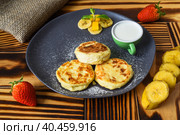 Syrniki or cheese pancakes with cream sauce and bananas on a plate on wooden table close up. Стоковое фото, фотограф Татьяна Терехина / Фотобанк Лори