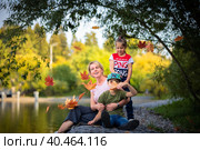 Mom with children is sitting by the pond in the park, autumn leaves are falling from above. Russia Moscow September 24, 2020. Редакционное фото, фотограф Юрий Поздников / Фотобанк Лори