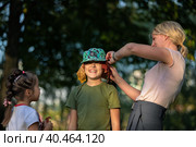 Mom plays with children in the park, puts leaves under her hat. Russia Moscow September 24, 2020. Редакционное фото, фотограф Юрий Поздников / Фотобанк Лори