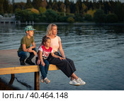 Mom with children sits on the pier by the pond at sunset. Russia Moscow September 24, 2020. Редакционное фото, фотограф Юрий Поздников / Фотобанк Лори
