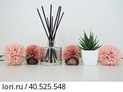 Composition of pink artificial flowers, incense sticks in a glass vase with essential oil. Still life on a white table. Aloe flower in a white pot. Room and apartment decor, interior design. Стоковое фото, фотограф Юлия Петровская / Фотобанк Лори