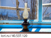 Used flat-wick kerosene lamp (also known as a paraffin lamp) on old shabby blue windowsill in the sunlight. Стоковое фото, фотограф Татьяна Терехина / Фотобанк Лори