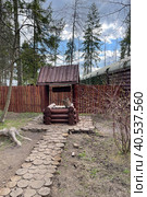 Antique wooden water well. Old wooden well.Old wooden wheel and bucket of water inside on grass ground, primitive knowhow. "Partisan village". Military-patriotic park "Patriot", Kubinka stock photo. Редакционное фото, фотограф Екатерина Казначеева / Фотобанк Лори