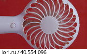 A man presses the power button on a portable portable fan. Demonstrates operating modes, then turns off. The propeller gradually stops. On a coral background. Close-up. Стоковое видео, видеограф Vadzim Yakubovich / Фотобанк Лори