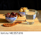 Cups with a traditional oriental pattern with dates and walnuts, a glass of clear water, stone rosary on the table during sunset. Стоковое фото, фотограф Ирина Кононова / Фотобанк Лори