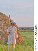 An senior Muslim man in a skullcap and traditional clothes leaves with a hand scythe from the hay field at sunset. Стоковое фото, фотограф Ирина Кононова / Фотобанк Лори