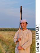 Portrait of smiling senior muslim man in an embroidered skullcap and white traditional clothes with hand-scythe in a hayfield. Стоковое фото, фотограф Ирина Кононова / Фотобанк Лори