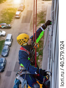 Professional industrial mountaineer worker washing exterior glazing, hanging over building. Rope access laborer climbing on wall fasade. Dangerous urban works concept. Copy advertising text space. Стоковое фото, фотограф Aleksandr Golubev / Фотобанк Лори