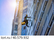 Professional industrial mountaineer worker washing exterior facade glazing, hangs over building, view from below. Rope access laborer climbing on wall house. Urban works concept. Copy ad text space. Стоковое фото, фотограф Aleksandr Golubev / Фотобанк Лори