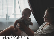Loving mother happy having fun with newborn baby on hands at home, lifestyle. Smiling mom with infant child indoors. Mum care 6 months old kid. Concept of motherhood, maternity. Copy ad text space. Стоковое фото, фотограф Aleksandr Golubev / Фотобанк Лори