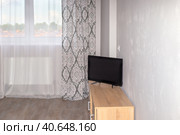 Bright room with a curtained window, a cabinet with a TV near a gray wall. Interior of a small living room, bedroom. Стоковое фото, фотограф Коханова Наталья / Фотобанк Лори