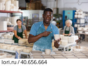 Portrait of african american worker cutting burrs off freshly made earthenware cups and plates with knife. Стоковое фото, фотограф Яков Филимонов / Фотобанк Лори