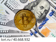 Золотая монета криптовалюты Биткоин лежит на сто-долларовых банкнотах США. Стоковое фото, фотограф Николай Винокуров / Фотобанк Лори