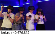Cheerful emotional young girls and guys in VR headsets fully immersed in game, actively engaged in virtual reality world, manipulating objects or shooting targets with joysticks in hands. Стоковое видео, видеограф Яков Филимонов / Фотобанк Лори