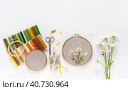 Summer needlework. Hand embroidery with satin ribbons of blooming daisies in round wooden hoop, sets of colorful ribbons, accessories for embroidery on white background. Flat lay, copy space, closeup. Стоковое фото, фотограф Виктория Катьянова / Фотобанк Лори