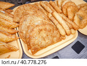 Вкусные свежие жареные чебуреки и сосиски в тесте на подносе в магазине. Чебуреки — это уличная еда, в которой между жареным тестом зажата начинка из приправленного мясного фарша. Стоковое фото, фотограф FotograFF / Фотобанк Лори