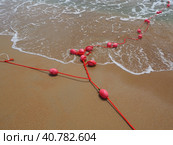Buoys on a rope in sea water. The lifebuoys are pink restraints to alert people to the depth of the water. Rescue of the drowning. Delimiting a place on sandy beach between hotels. Wave with bubbles. Стоковое фото, фотограф Юлия Петровская / Фотобанк Лори