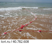 Buoys on a rope in sea water. The lifebuoys are pink restraints to alert people to the depth of the water. Rescue of the drowning. Delimiting a place on sandy beach between hotels. Wave with bubbles. Стоковое фото, фотограф Юлия Петровская / Фотобанк Лори