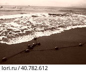 Buoys on a rope near sea water. The buoys are bright pink restraints to alert people to the depth of the water. Sepia. Delimiting a place on a sandy beach between hotels. Waves with bubbles. Стоковое фото, фотограф Юлия Петровская / Фотобанк Лори
