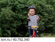 A cheerful little boy rides a running bike in a helmet outdoors. A happy child is engaged in an active sport. Protection. Life insurance and child safety. Стоковое фото, фотограф Photojuli / Фотобанк Лори
