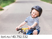 A cheerful little boy rides a running bike in a helmet outdoors. A happy child is engaged in an active sport. Protection. Life insurance and child safety. Стоковое фото, фотограф Photojuli / Фотобанк Лори