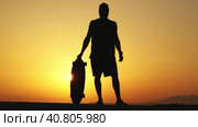 Silhouette of a man standing on sunset holding a longboard. Стоковое видео, видеограф Константин Шишкин / Фотобанк Лори