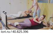 Two health conscious women of different ages perform a Pilates exercise using a reformer bed, where a female instructor helps them do it correctly. Стоковое видео, видеограф Яков Филимонов / Фотобанк Лори