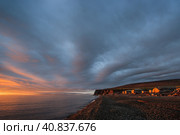 Summer sunrise on the coast of the Arctic Ocean. The coast and houses are illuminated by the sun. Clouds in the sky. Uelen village, Chukotka Peninsula, Chukotka, Far East of Russia. Chukchi Sea. Стоковое фото, фотограф Андрей Степанов / Фотобанк Лори
