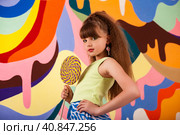 Pretty little girl 9-10 year old holding round large lollipop at colored wall, pensive looking at camera. Cute kid in yellow t-shirt with big candy on stick. Summer fashion concept. Copy ad text space. Стоковое фото, фотограф Aleksandr Golubev / Фотобанк Лори