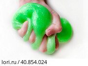 Hand Playing with textured slime with bubbles, stretching the gooey substance. Female teen hand holding green shining slime, squeezing it. Adorable Girl stretching slime toy to the sides. Liquid toy. Стоковое фото, фотограф Марина Демидюк / Фотобанк Лори