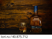 A bottle Nucky Thompson Blended Scotch Whisky and a glass with ice on a dark wooden background. The whiskey has a bright, rounded taste with hints of walnuts and honey. (2021 год). Редакционное фото, фотограф Воловодов Владимир / Фотобанк Лори