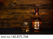 Bottle of Chivas Regal Scotch Whisky 12 years old and a glass with ice on a dark wooden background. A leader among premium blended Scotch whiskies. (2021 год). Редакционное фото, фотограф Воловодов Владимир / Фотобанк Лори
