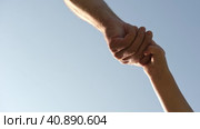 Adult holding a child by the hand on blue sky background. Parent hand reaches out to help child hand in need. Kids Shaking Hands. Children's hand reaches for a daddy. family united. Handshake. Стоковое видео, видеограф Марина Демидюк / Фотобанк Лори