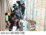 Industry mountaineer laborers in uniform and helmets hangs over residential building facade. Two workers working on wall house, access high rise work. Industrial urban work concept. Copy ad text space. Стоковое фото, фотограф Aleksandr Golubev / Фотобанк Лори