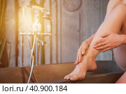 Pretty woman sitting putting massage oil on legs skin in bathroom, close-up photo. Lovely young lady smoothes cosmetic oil on leg at bath. Cosmetology self care concept. Copy advertising text space. Стоковое фото, фотограф Aleksandr Golubev / Фотобанк Лори