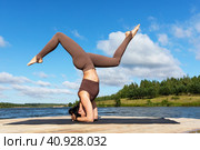 A woman practicing yoga, performs a variation of the Shirshasana exercise, inverted asana, headstand and handstand, trains in sportswear on the shore of a lake on a warm sunny morning. Стоковое фото, фотограф Сергей Чайко / Фотобанк Лори