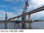 Портовый кран на Гутуевском острове в городе Санкт-Петербурге осуществляет погрузку на судно «Борис Марисов». Вид с Канонерского острова (2023 год). Редакционное фото, фотограф Румянцева Наталия / Фотобанк Лори