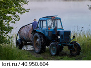 Blue wheeled agricultural tractor with tank trailer is refueled with water from forest lake. Стоковое фото, фотограф Владимир Григорьев / Фотобанк Лори