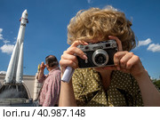 Девушка в одежде времен 1960-х годов фотографирует советским фотоаппаратом Зоркий-6 на площади Промышленности на ВДНХ в городе Москве, Россия (2023 год). Редакционное фото, фотограф Николай Винокуров / Фотобанк Лори