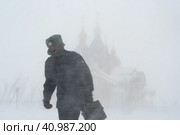 Российский полицейский идет по городу во время сильной метели. Ветреная и снежная погода. Снежная буря и пурга в городе. Вдали собор. Анадырь, Чукотка, Россия. Редакционное фото, фотограф Андрей Степанов / Фотобанк Лори