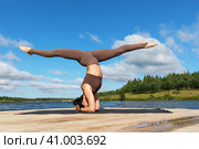 A woman practicing yoga performs the Sirshasana exercise with Hanumanasana, an inverted asana with a longitudinal twine, trains in sportswear on the shore of a lake on a warm sunny morning. Стоковое фото, фотограф Сергей Чайко / Фотобанк Лори
