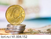 Деньги. Монета номиналом в 10 рублей на стопке монет в 1 рубль. На фоне 100-рублевых купюр. Стоковое фото, фотограф E. O. / Фотобанк Лори