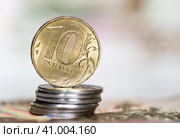 Деньги. Монета номиналом в 10 рублей на стопке монет в 1 рубль на фоне 100-рублевых купюр. Стоковое фото, фотограф E. O. / Фотобанк Лори