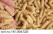 Hand Pouring Gluten Free Cornmeal Pasta. Spiral Raw Macaroni from Blend of Corn and Rice flour rotating on Turntable. Top View. Close Up. Uncooked Rotini Pasta is Spinning. Food Background. Ad. Стоковое видео, видеограф Марина Демидюк / Фотобанк Лори