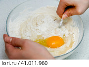 Woman's hands with an yeast dough. The woman has added the yolk of a chicken egg and is stirring the baking dough in a glass bowl. Женские руки с дрожжевым тестом. Женщина добавила желток куриного яйца и замешивает тесто для выпечки в стеклянной миске. Стоковое фото, фотограф Дмитрий Березнев / Фотобанк Лори