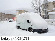 Автомобиль покрыт снегом после снегопада. Сугробы кругом на дороге и во дворе. Снег на крыше и лобовом стекле автомобиля. На заднем плане панельные дома и сопка. Город Магадан, Магаданская область, Россия. Стоковое фото, фотограф Андрей Степанов / Фотобанк Лори