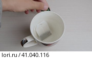 A man places a black tea bag in a white ceramic mug on the kitchen table. View from above. Стоковое видео, видеограф Алексей Гекало / Фотобанк Лори